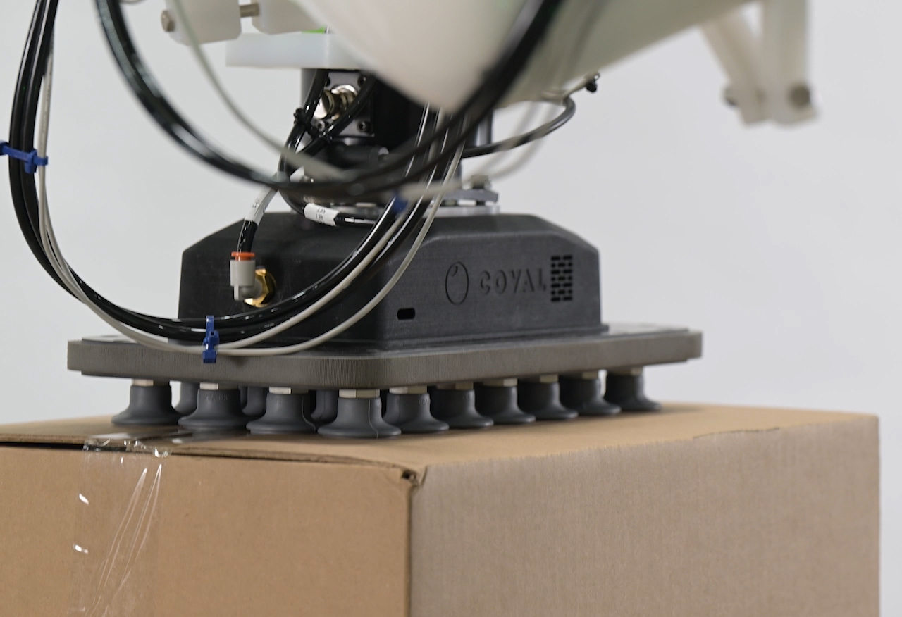 Vacuum Suction Cup Gripper End Effector Gripping Cardboard Box close-up of a Coyal vacuum suction cup gripper attachment on a robotic arm gripping the top of a cardboard box